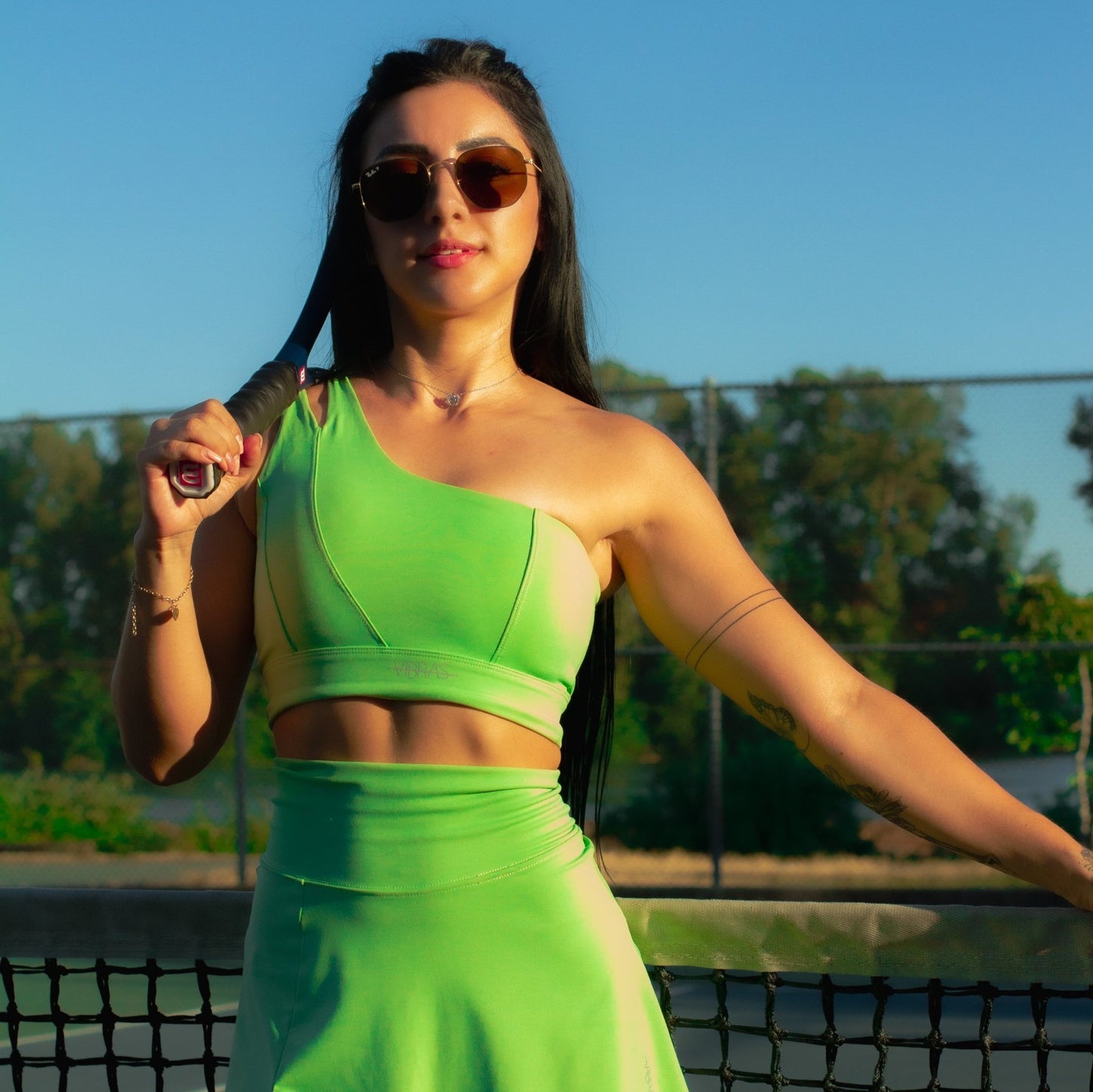 Fitness model posing with a racquet on a tennis court wearing a green apple, mini skort matching set from vibras activewear.