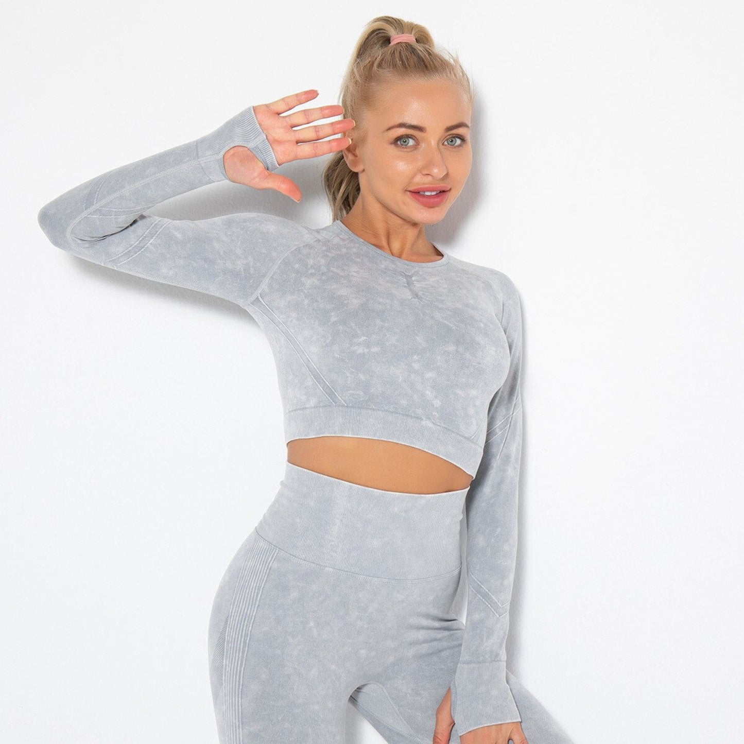 FITNESS MODEL STRETCHING IN ARIA WORKOUT CROP TOP IN GREY FEATURING THUMBHOLES ON SLEEVES, FROM VIBRAS ACTIVEWEAR.