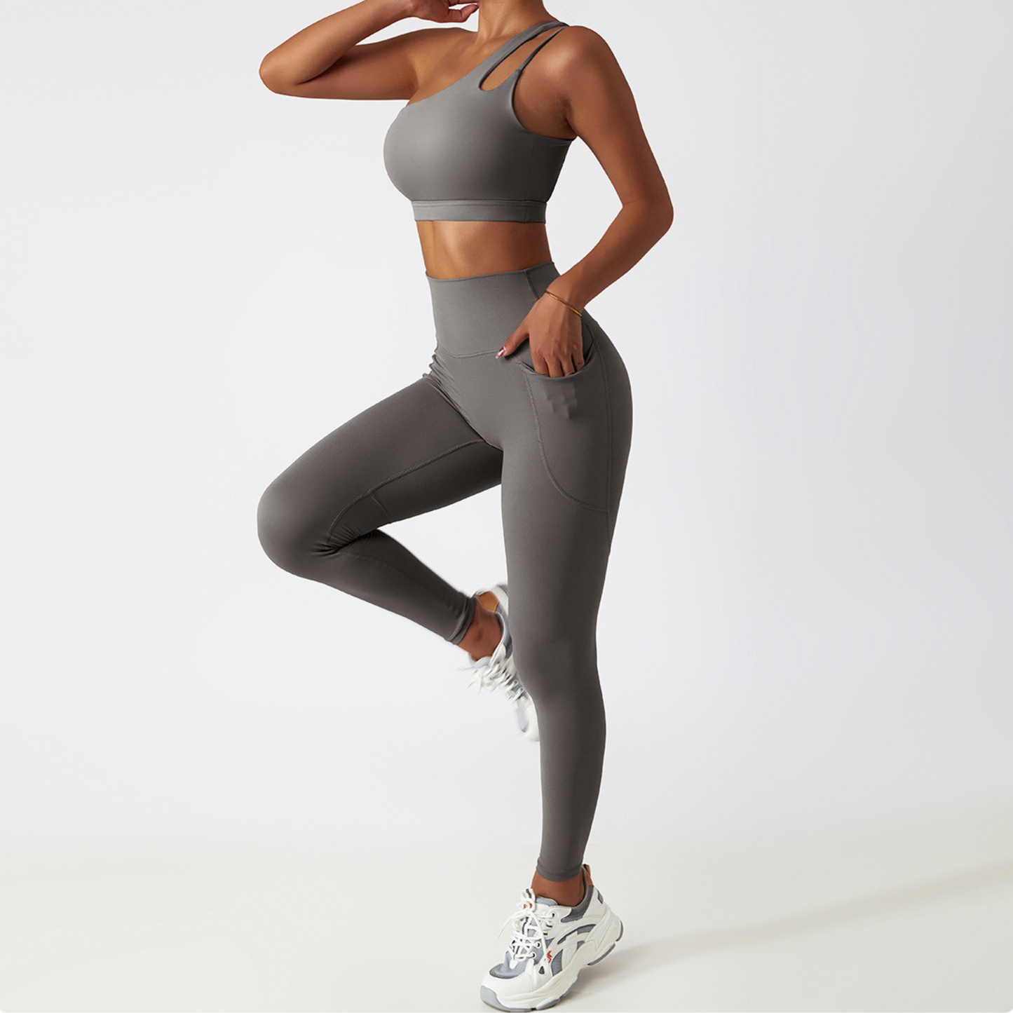 Fitness model wearing a one shoulder, sexy and squat proof matching set in the colour grey from vibras activewear.